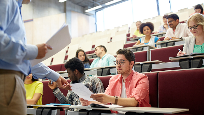 A teacher is handing back tests to students in a lecture theatre 