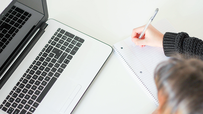 A student makes notes as she works on an expensive laptop.