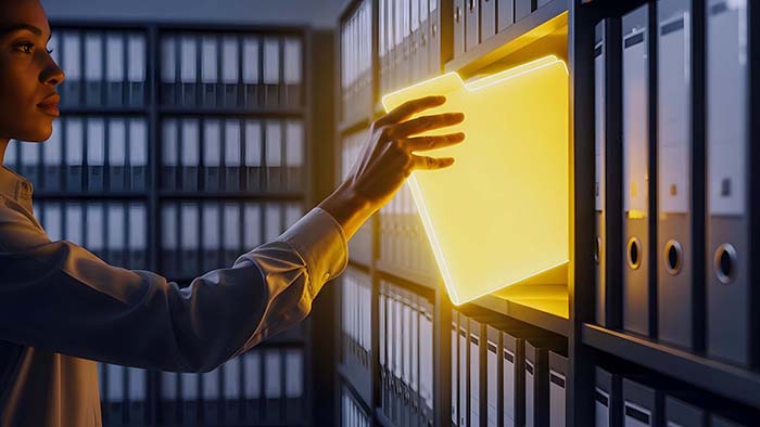 A woman places a glowing folder on to a row of well maintained non-glowing folders to represent safely storing digital information.
