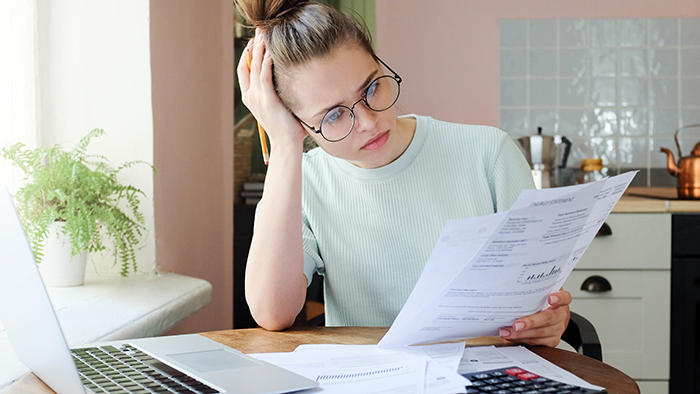 A woman by a laptop, working from home and concentrating on a pile of papers in her hand.