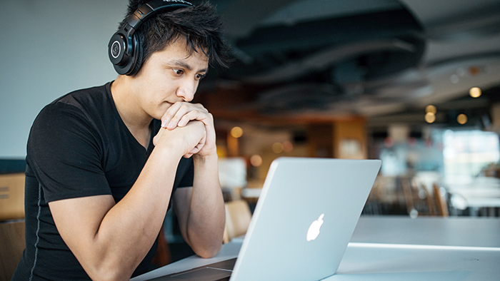 A student with headphones on watches something, or reads something, on a computer screen.