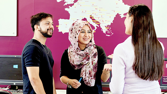 Three smiling students working together in front of a map of Europe.