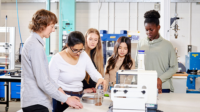 Five engineering pr medical students gathered around some kind of hi-tech laboratory device.