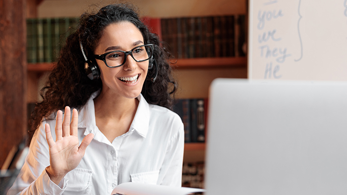 A young adult smiling and waving at a computer