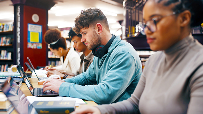 A row of students working in a library. some have headphones around their necks.