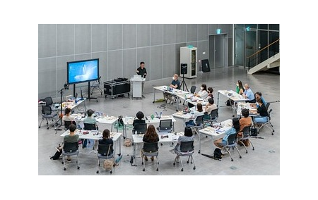 An image of students sat at desks in a horseshoe shape looking at a screen