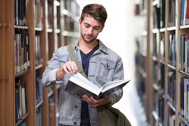 Image of a male student in a library facing the camera looking down into a book