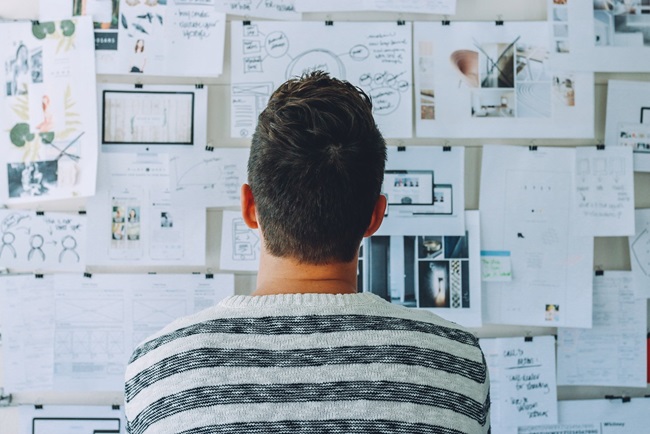 Image of a man looking at a noticeboard with lots of clips of primary research on