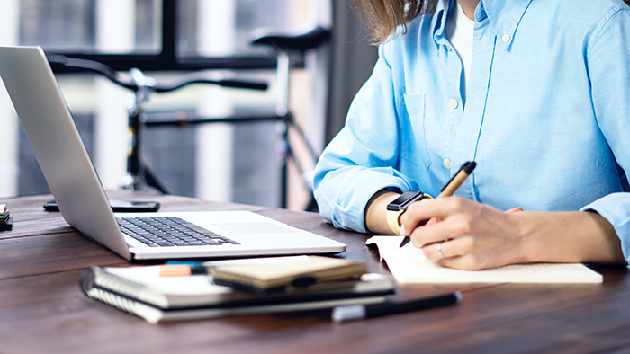 A woman writing on a notepad next to a laptop. 