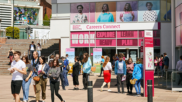 Lots of students congregating outside Owen Building on a sunny day. Behind them is the Careers Connect building.