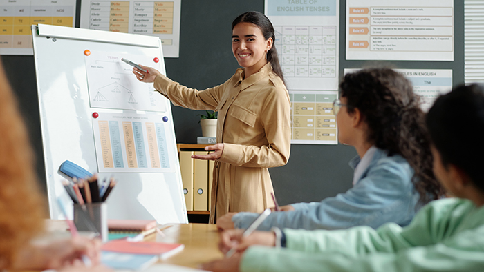 A young woman points to something on a flipchart stand, while a small number of people look on.