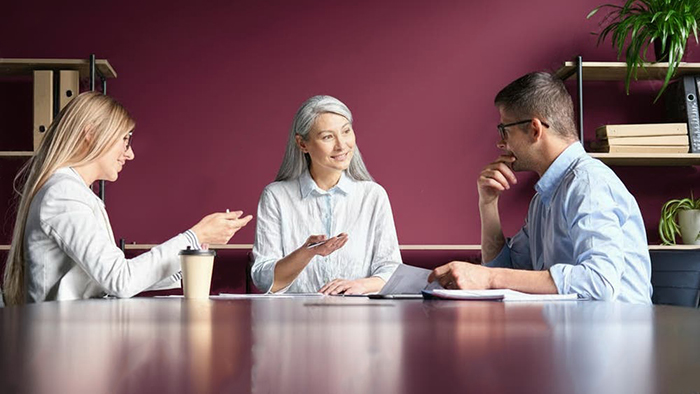 Three people sat at a table in an office in an animated discussion.