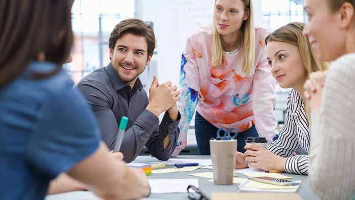 A group of young adults are working together around a table in a well-lit meeting room