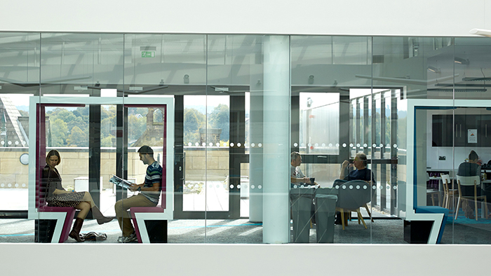 A view from outside a staff area showing a small kitchen and meetings areas, which are being used. 