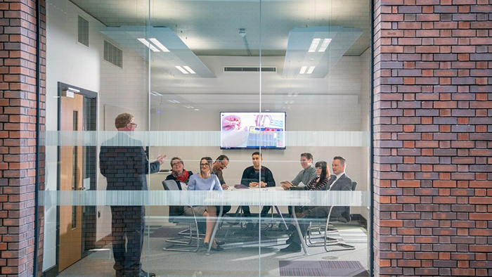 A view from outside a meeting room of a lecturer speaking in front of his peers  